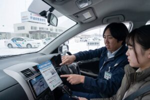 伊達自動車学校の教習車内でベテラン指導員から冬道運転のアドバイスを受ける様子