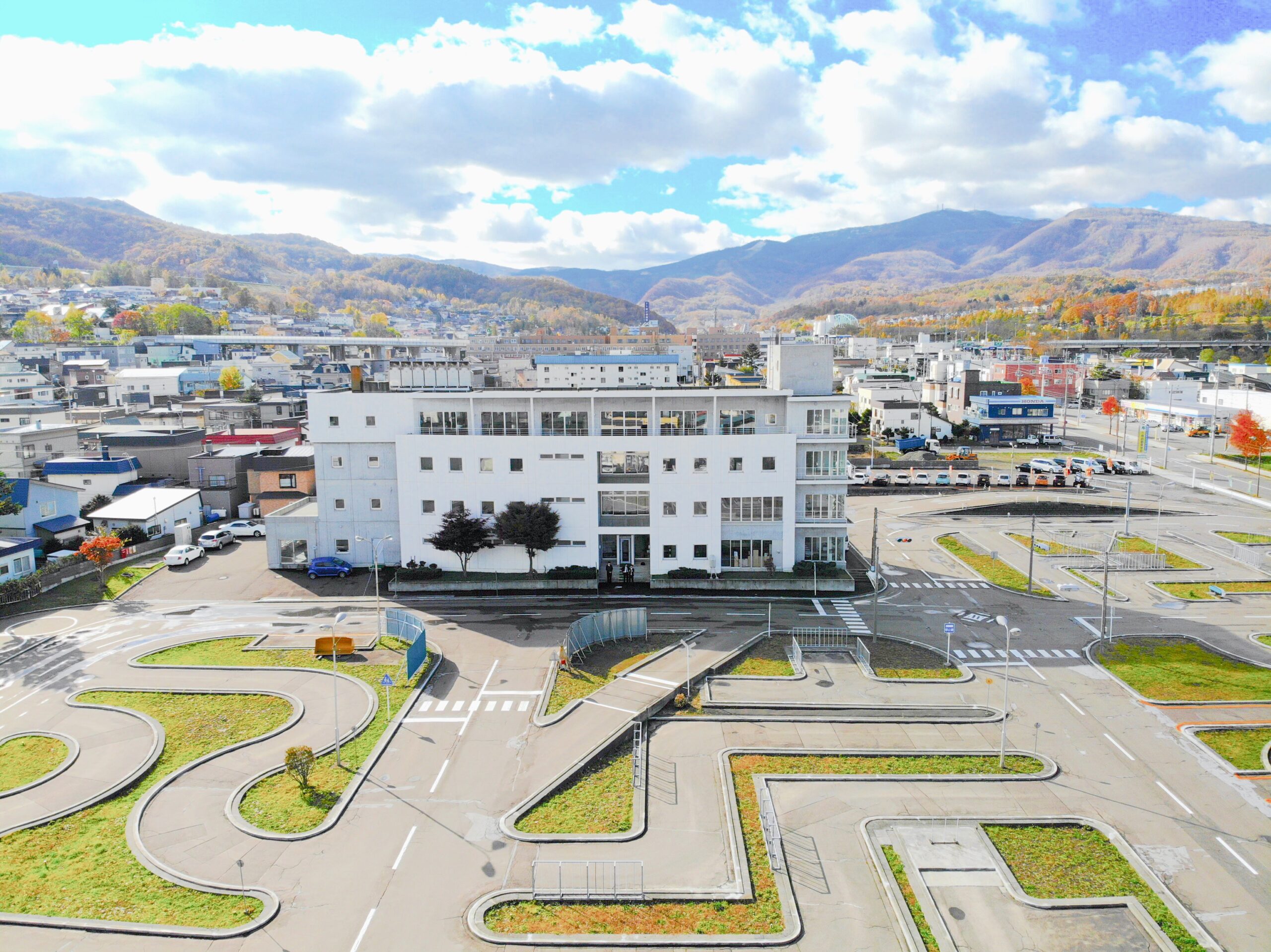 小樽自動車学校 校舎と教習コースの空撮写真。背景には北海道の山並みが広がる